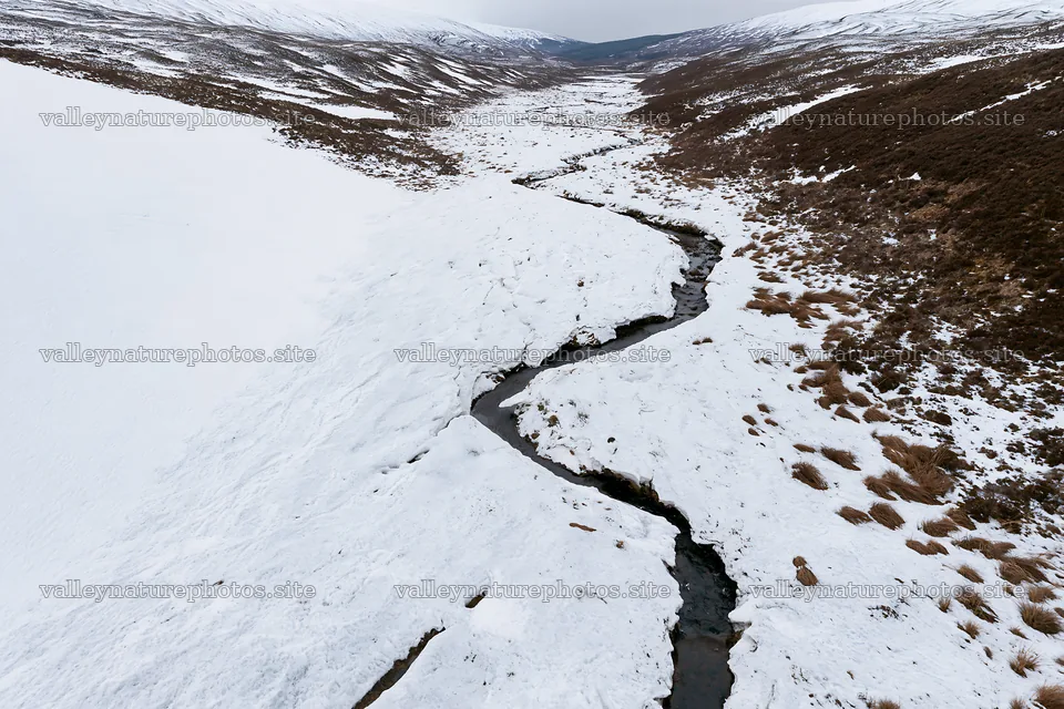 Aerial view of snowy meadow valley with stream – nature photography 9722x6480
