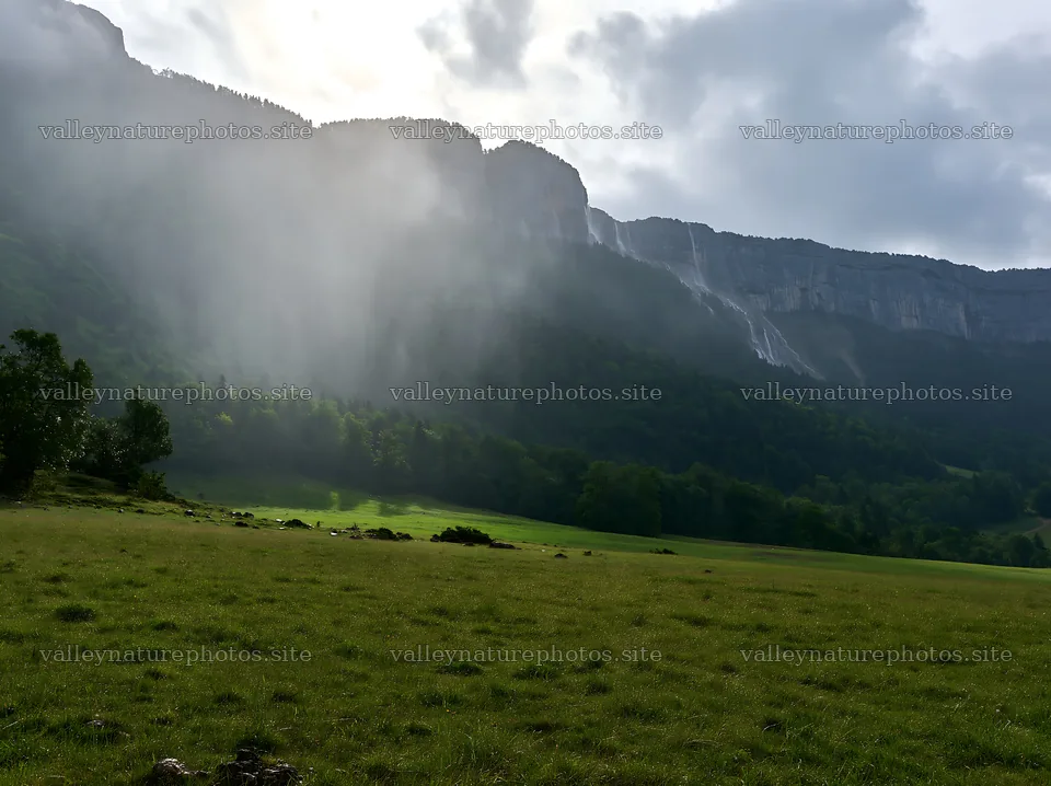 Meadow beneath crags with mist and waterfalls in the distance – nature photography 9174x6866