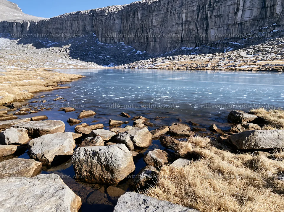 Frozen tarn in a meadow with rocks and cliffs nearby – nature photography 9174x6866